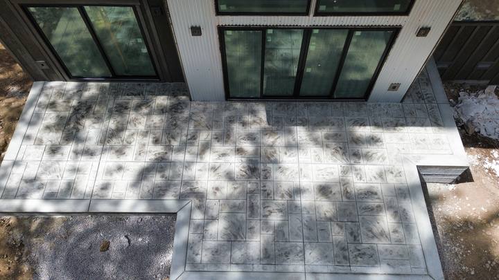Overhead view of a finished stamped concrete patio in an ashlar-slate pattern, wrapping the glass doors of a modern mountain home — Truckee area