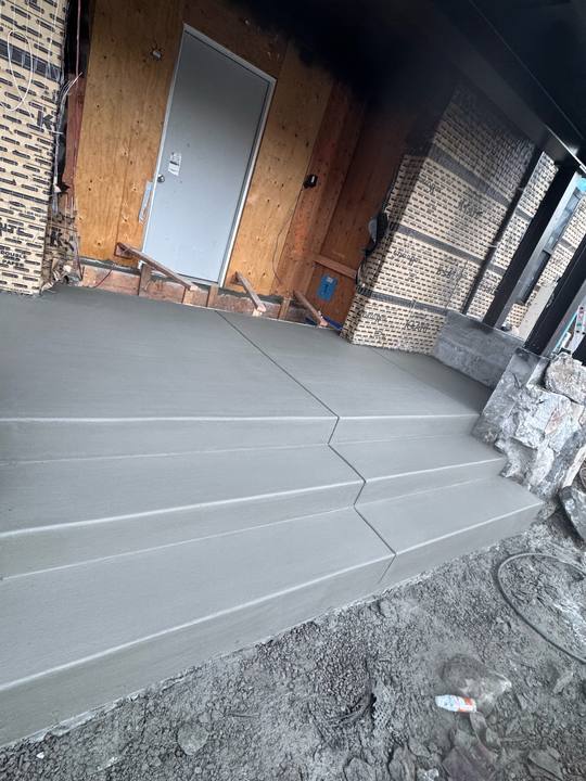 Freshly finished concrete steps and a landing poured up to a doorway, edges tooled and the top slab still green