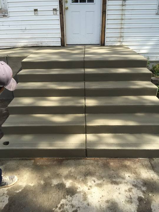 A newly poured five-riser concrete stoop at the back door of a white clapboard house, treads brushed for grip and edges run