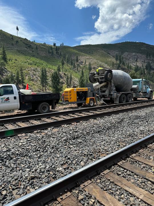 A concrete pump and mixer truck set up beside railroad track in a canyon — a pour with no road access for a truck chute