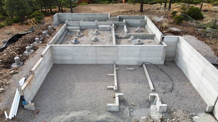 Overhead view of a completed foundation — stem walls stripped, interior footing pads poured, drain rock spread across the crawl space