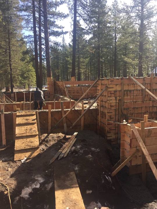 Foundation wall forms set and braced for a winter pour, snow still lying in the shade of the pines