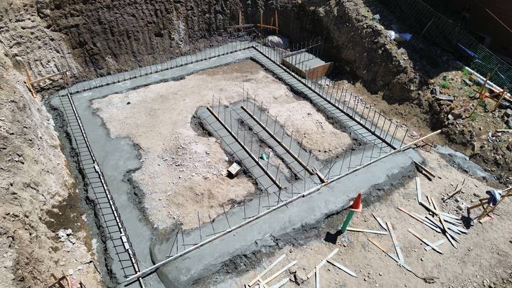 Overhead view of a poured perimeter footing with vertical rebar dowels left standing for the walls, in an open excavation