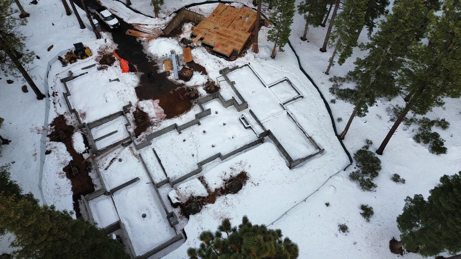 Overhead view of a completed foundation under a dusting of snow, the full footprint of walls poured and the framing started alongside — Truckee area