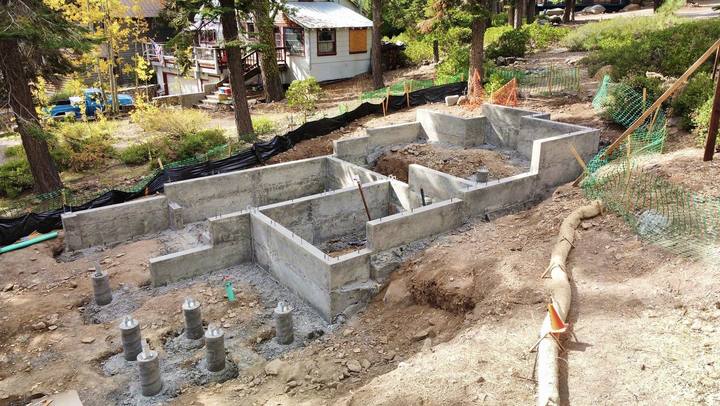 A stepped stem-wall foundation and pier pads on a sloping lot, poured tight beside an existing cabin