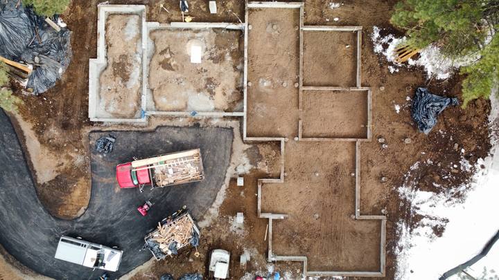 Straight-down view of a foundation in progress — footing trenches excavated on one half, walls already poured on the other